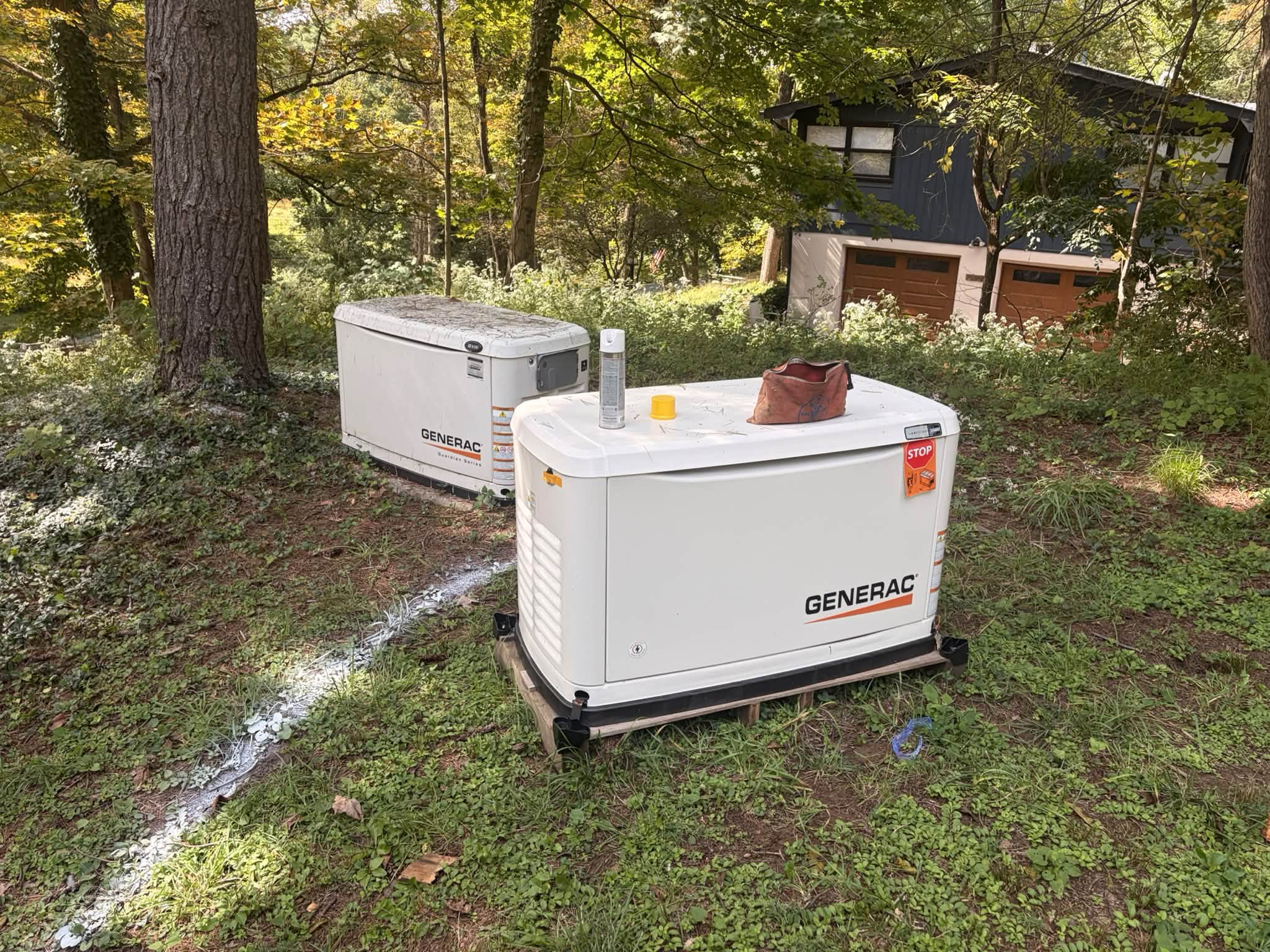 Two Generac generators at a wooded residential job site, with installation work in progress