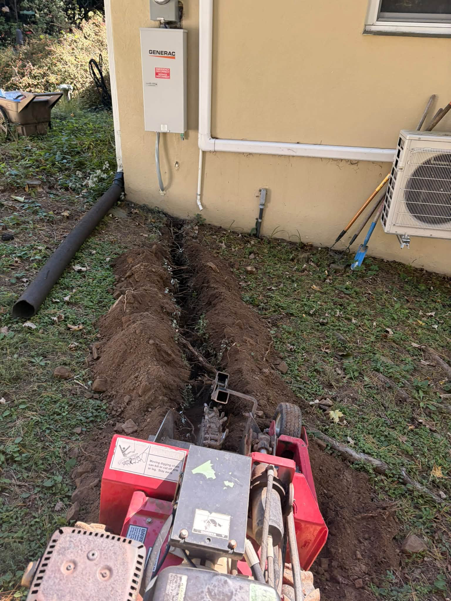 Trenching beside a home with Generac transfer equipment mounted on the wall. Work in progress.