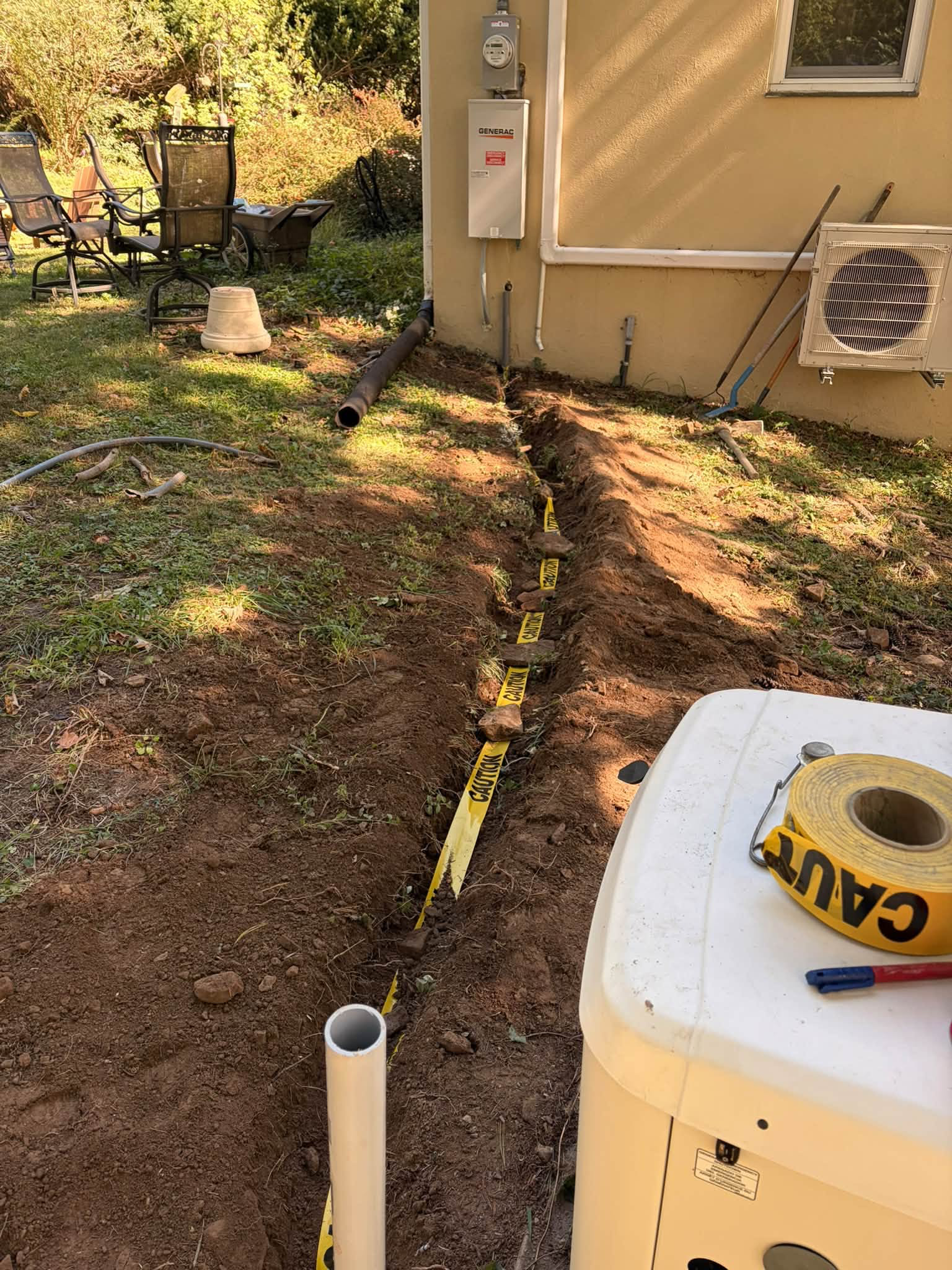An open trench with caution marking between generator equipment and the home. Work in progress.