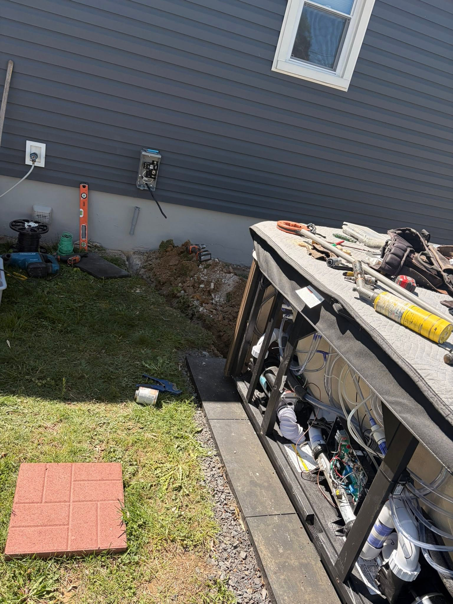 A hot tub with its service panel open and electrical work underway beside the home.