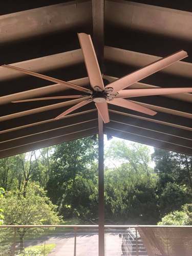 A large ceiling fan beneath an exposed-beam porch roof.